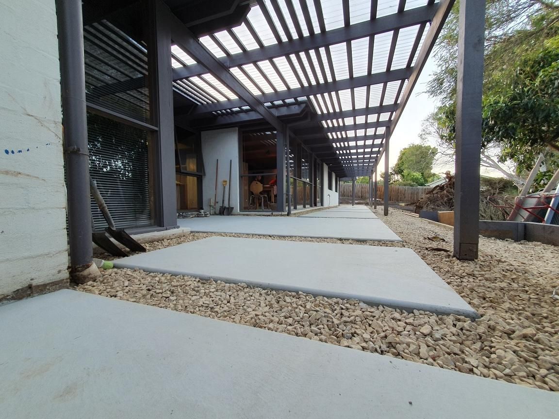 Modern house patio with concrete stepping stones, gravel, and a covered pergola walkway