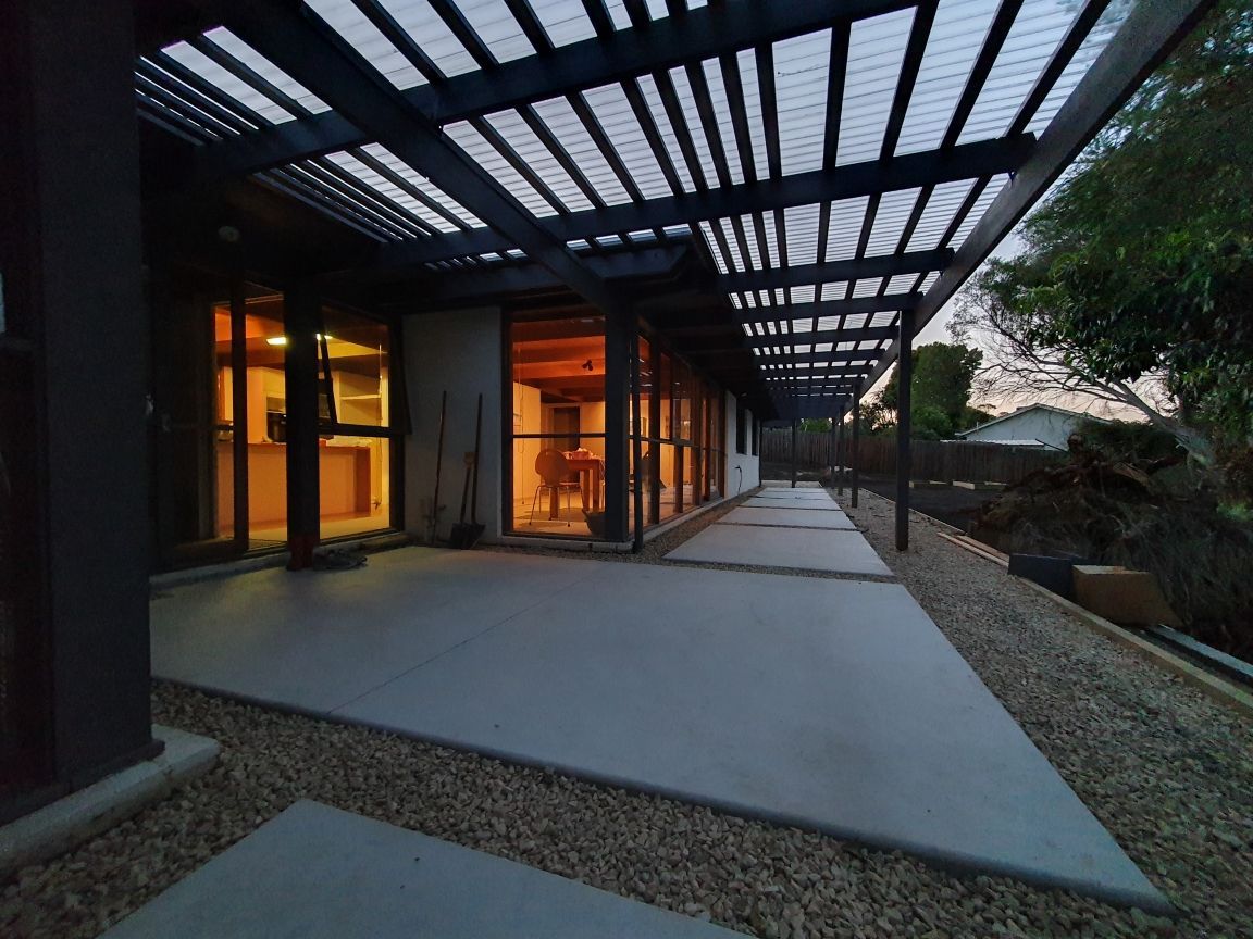 Covered outdoor walkway beside modern building at dusk, with glowing interior lights and geometric roof shadows