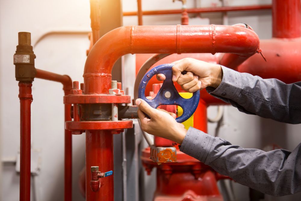 A Man is Fixing a Valve on a Red Pipe — J & N Plumbing Pty Ltd In Qurindi, NSW