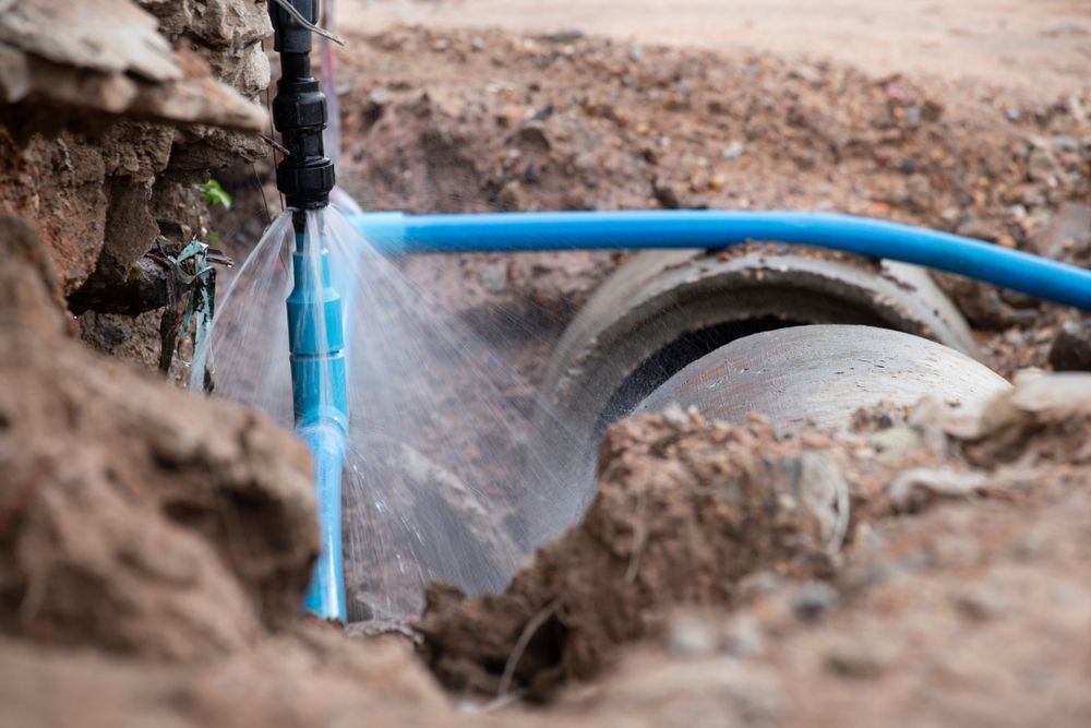 A Blue Pipe is Leaking Water Into a Concrete Pipe — J & N Plumbing Pty Ltd In Manilla, NSW