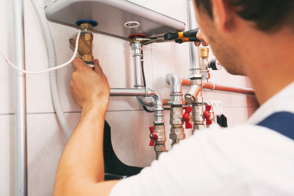 A Man is Fixing a Water Heater With a Wrench — J & N Plumbing Pty Ltd In Tamworth, NSW