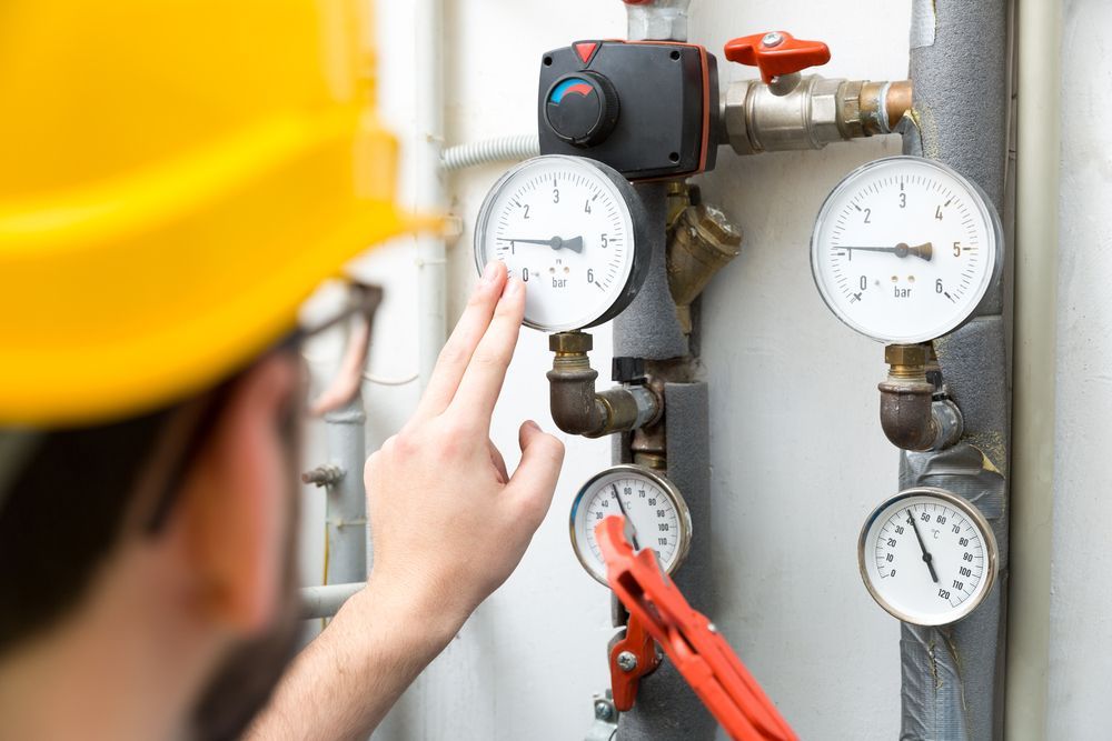 A Man in a Hard Hat is Adjusting a Pressure Gauge on a Pipe — J & N Plumbing Pty Ltd In Armidale, NSW