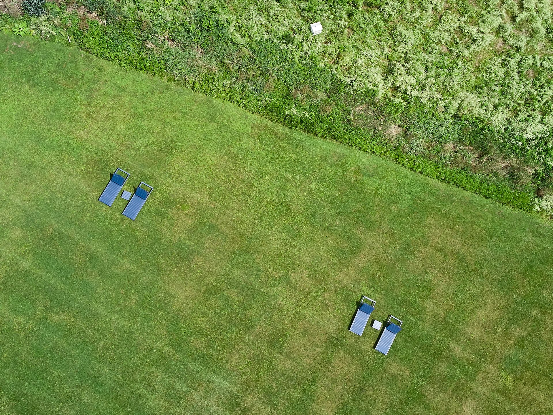 Two blue chairs on a grassy field near a hedge, viewed from above.
