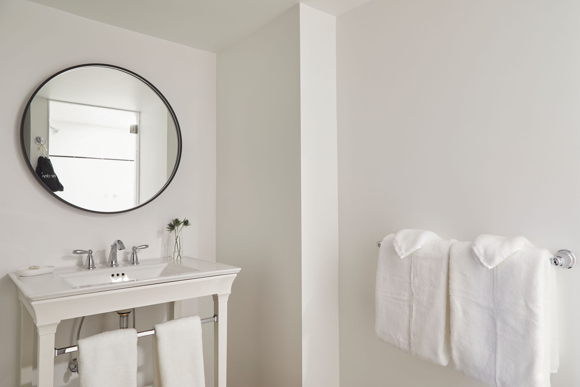 Minimal white bathroom with pedestal sink, round mirror, and towels on a wall rack