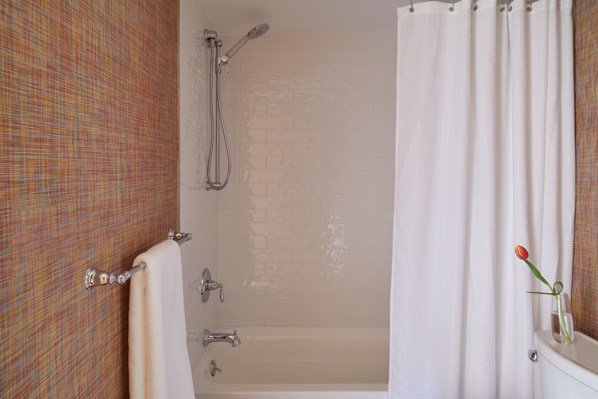 Small bathroom with a shower-tub, beige tile, white curtain, and a towel on the wall.