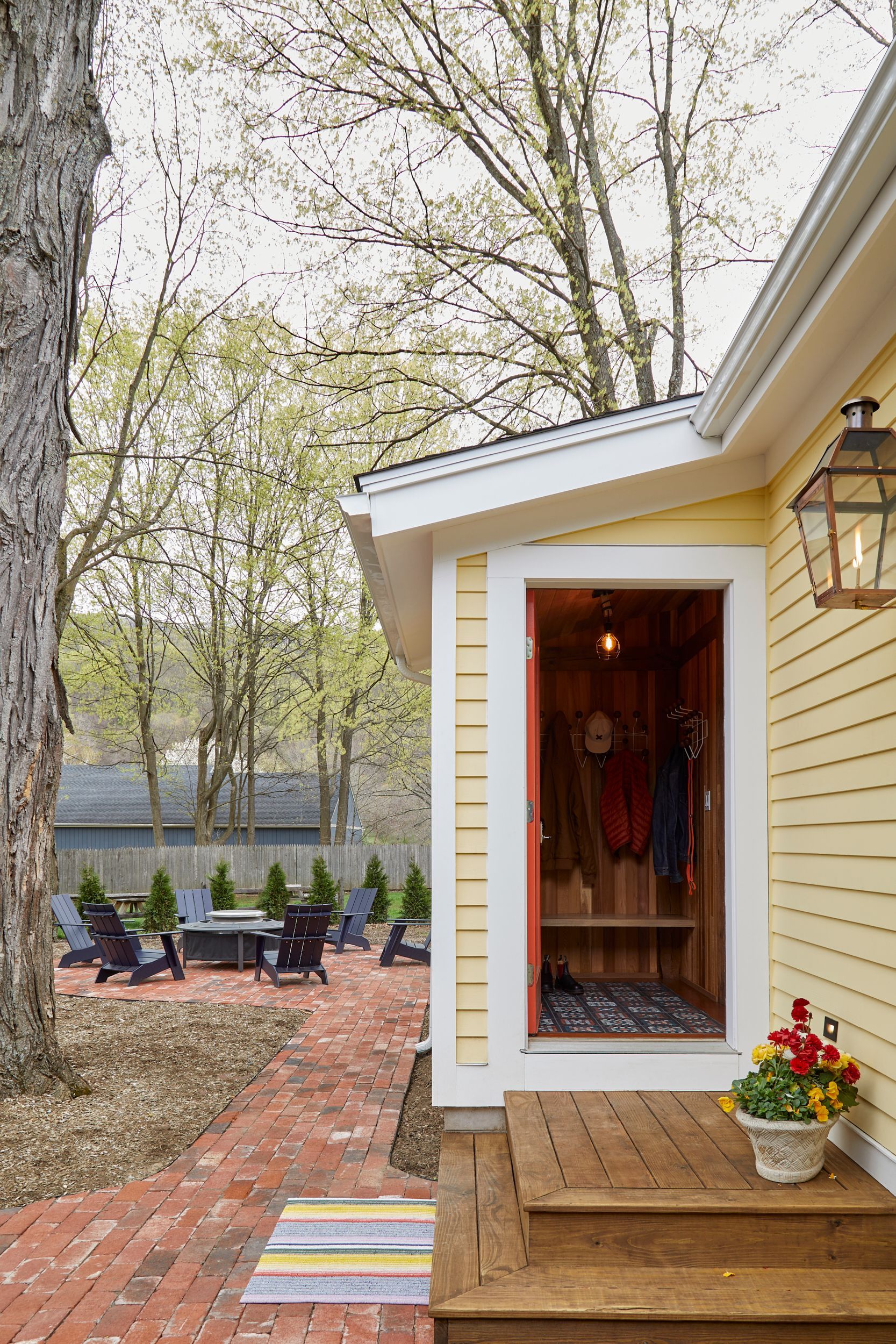 Yellow house entry with brick walkway, potted flowers, and a small porch by a wooded lakeside yard