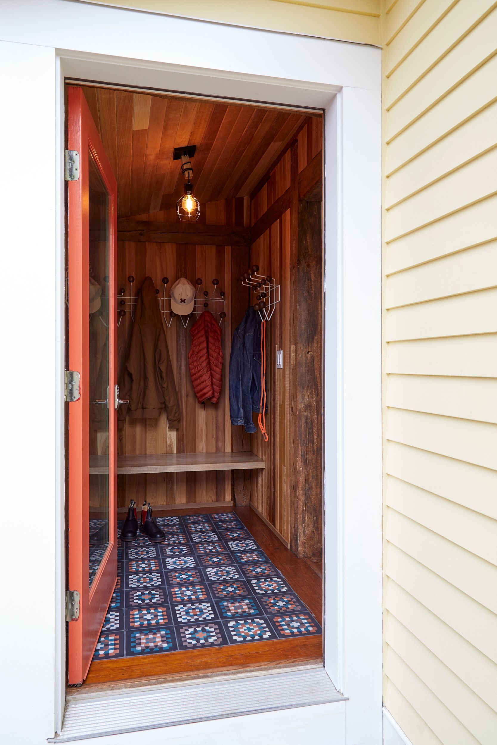 Small wooden porch closet with a patterned rug and hanging coats inside