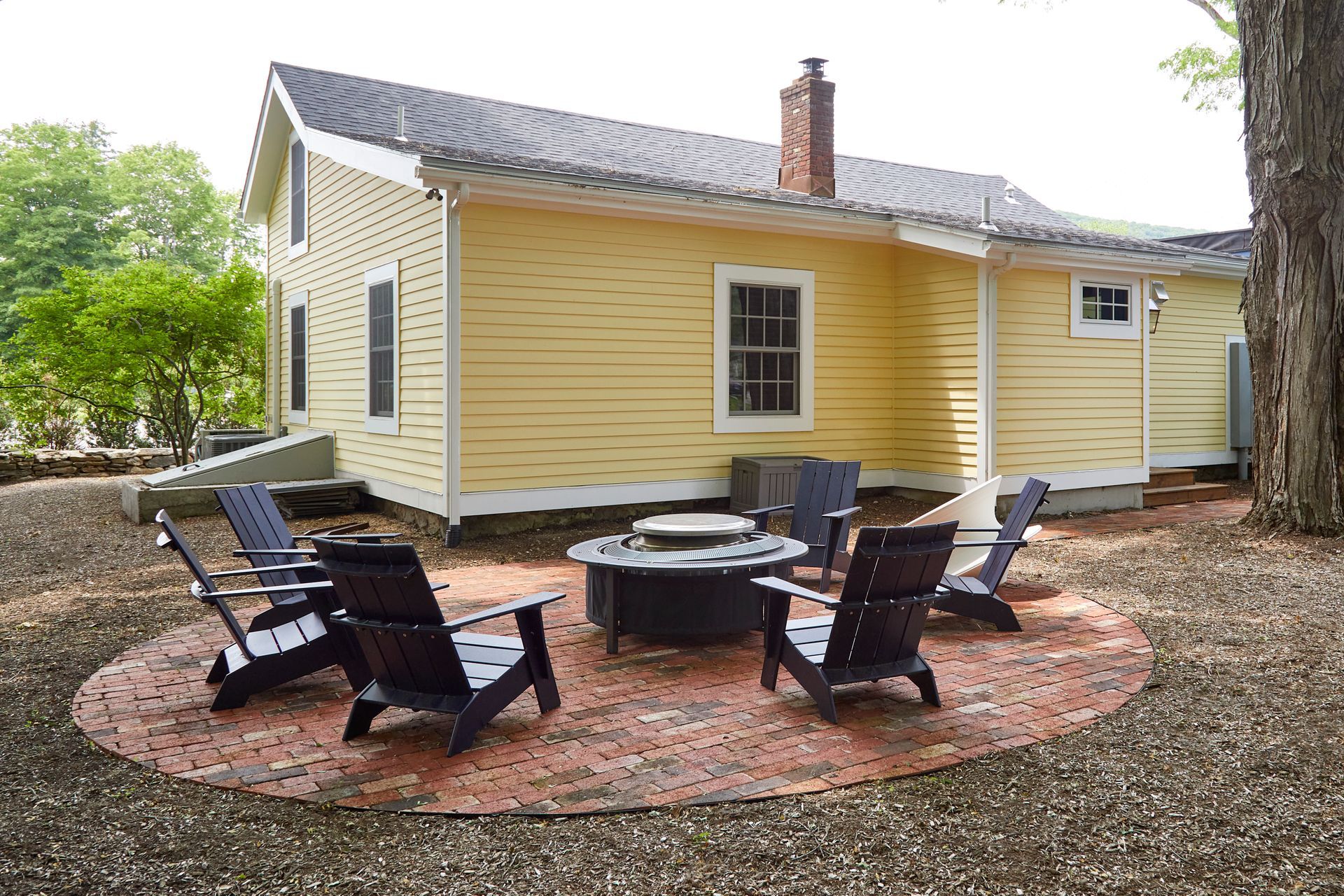 Yellow house patio with fire pit and four black chairs on a brick circle