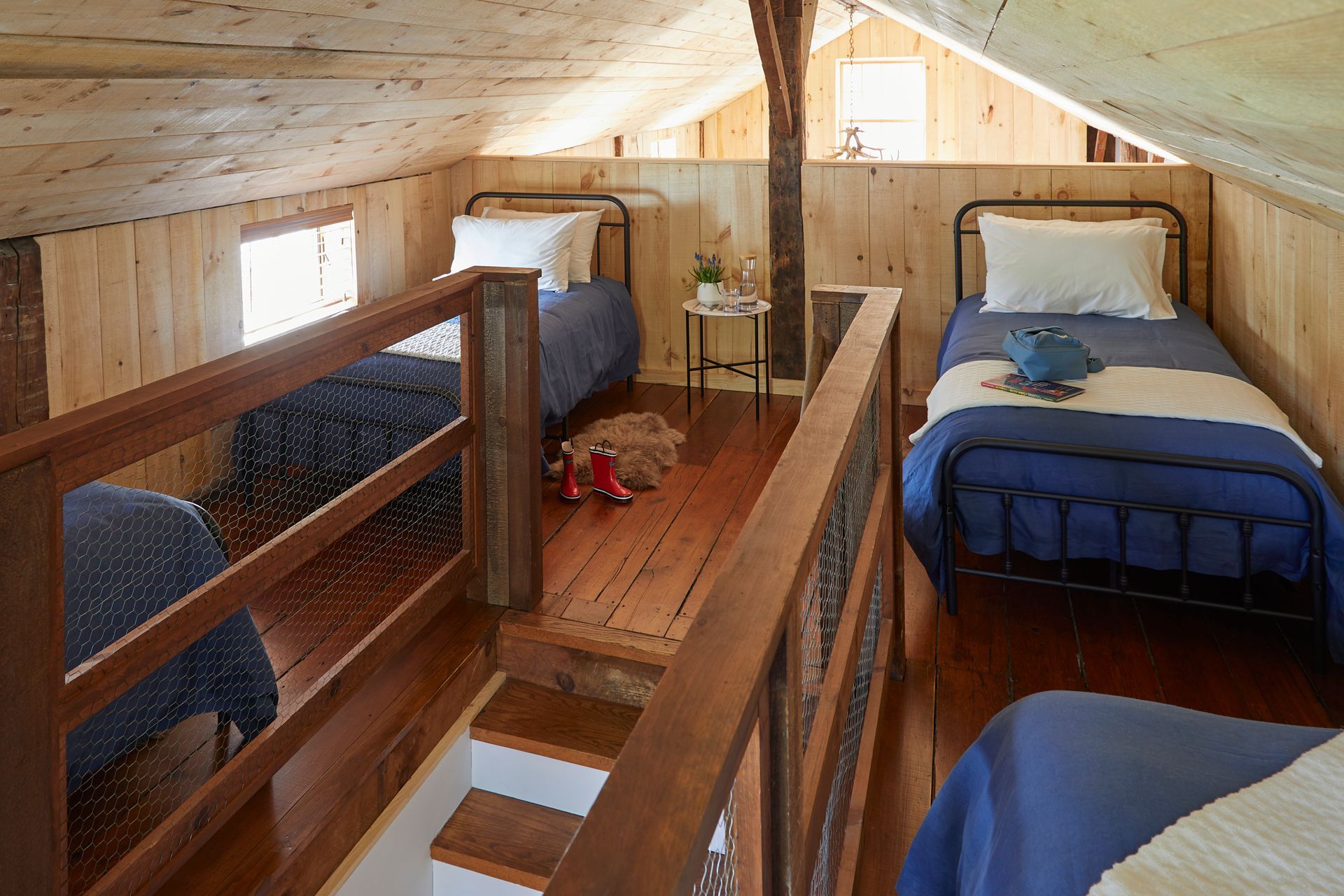 Dorm-style loft bedroom with three blue beds, wooden railings, and skylights.