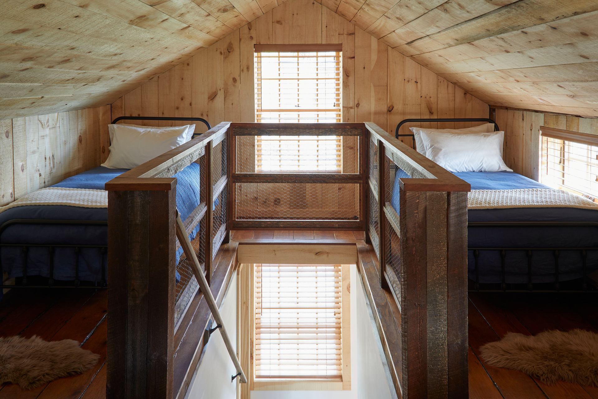 Wooden bunk room with two beds and a central skylight window reflected in a mirror.