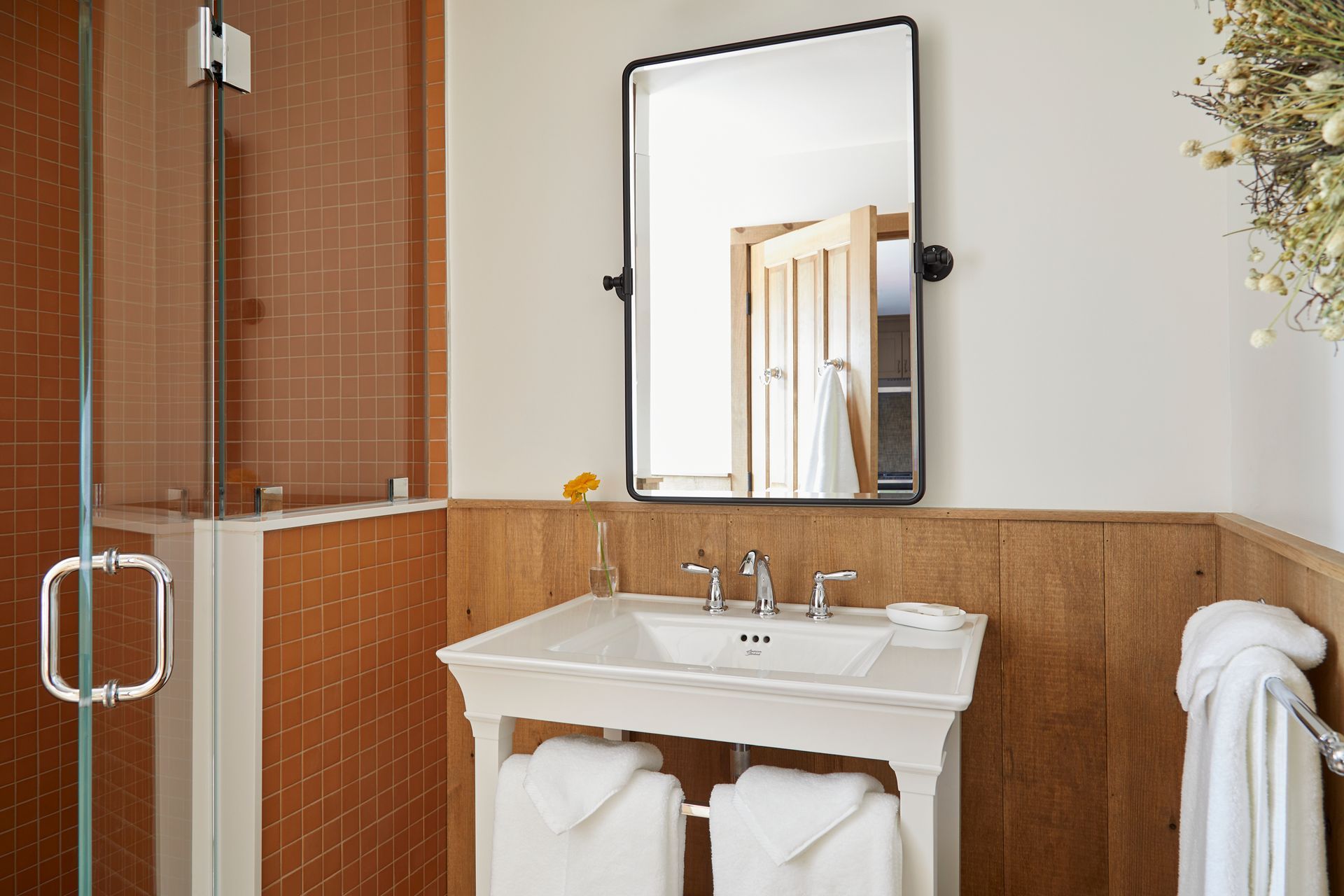 Modern bathroom with glass shower, white sink, and wood paneling
