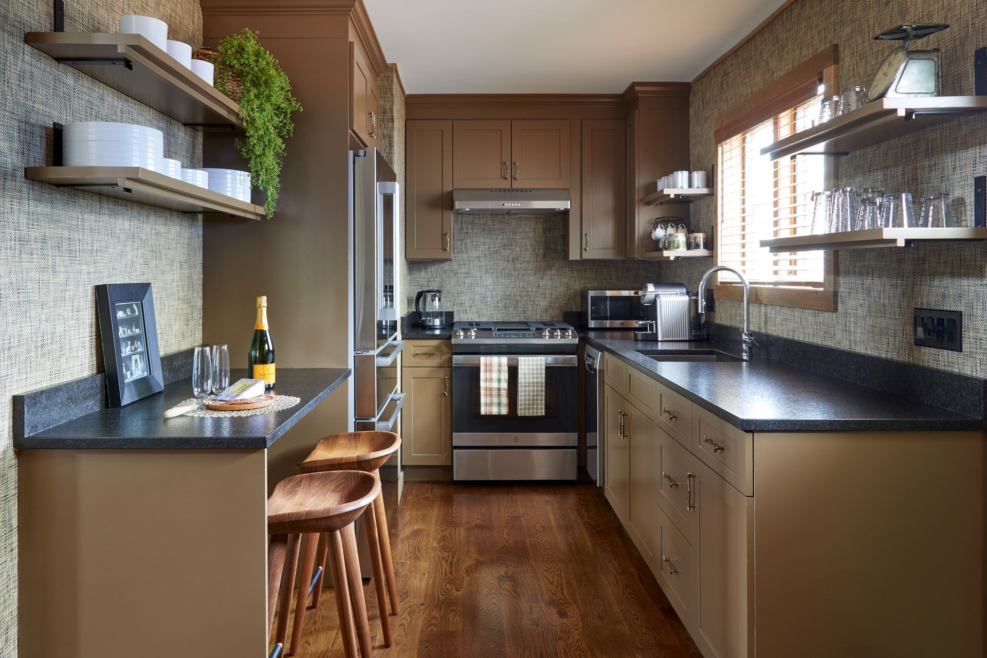Compact kitchen with wood cabinets, black countertops, and stainless steel appliances, lit by a large window.