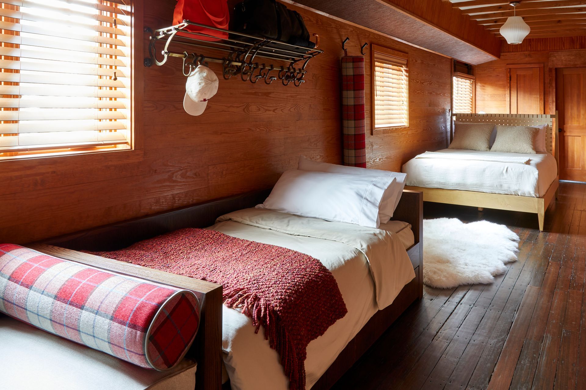 Wood-paneled sleeper cabin with two beds, wooden floors, and sunlight through small windows