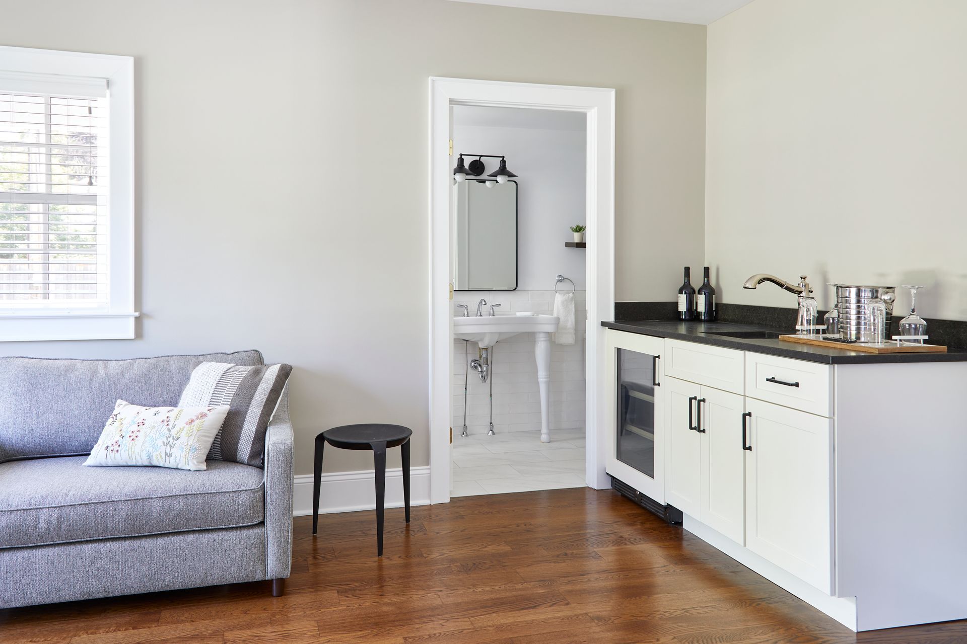 Bright living room with gray sofa, small stool, and kitchen pass-through with white cabinets and black countertop