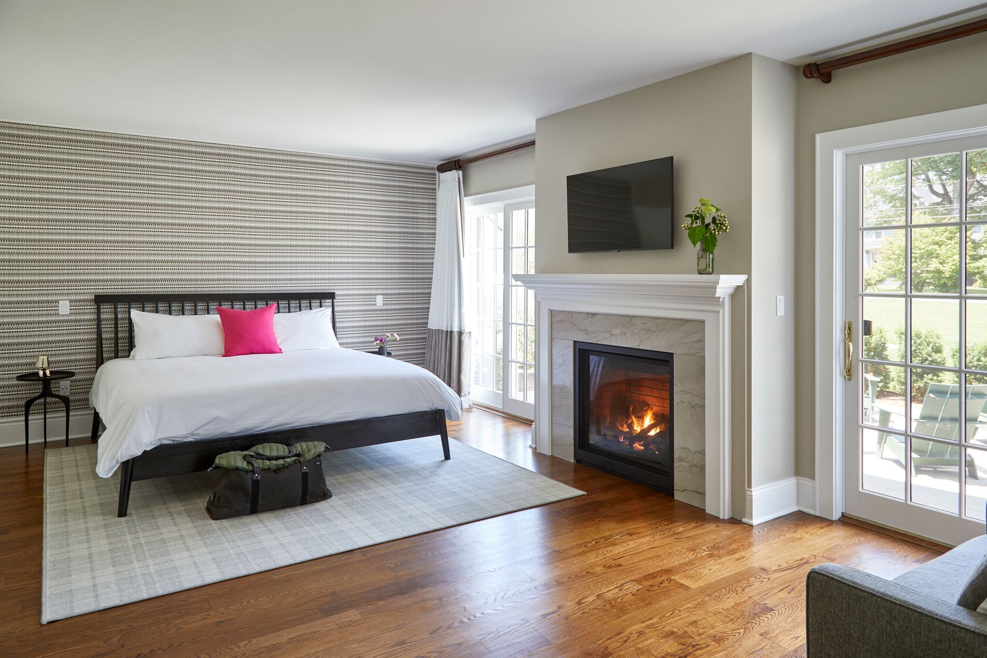 Bright bedroom with a fireplace, wall-mounted TV, bed, and sliding glass doors to a balcony.
