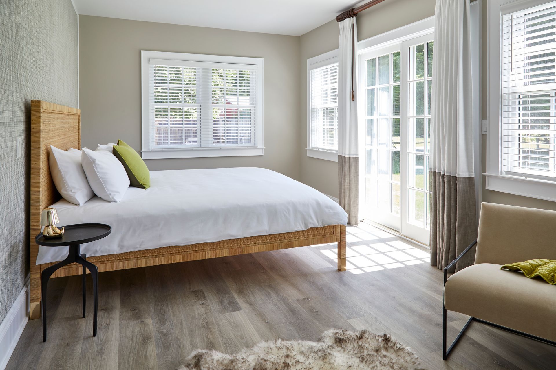Bright bedroom with a wooden bed, white bedding, large windows, and a chair by the open door.