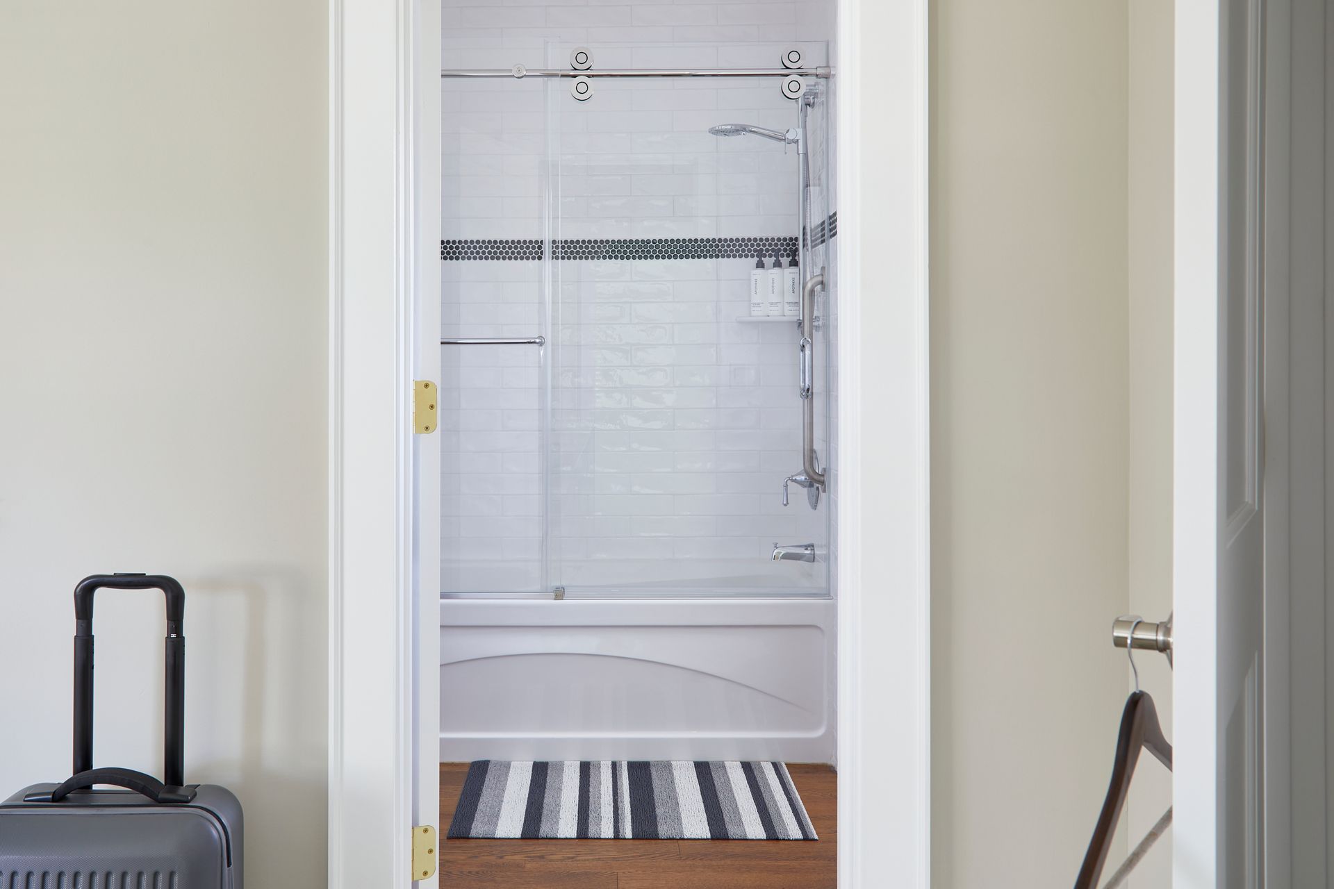 Bathroom doorway with a white tub, tiled shower, and striped rug visible beyond the door