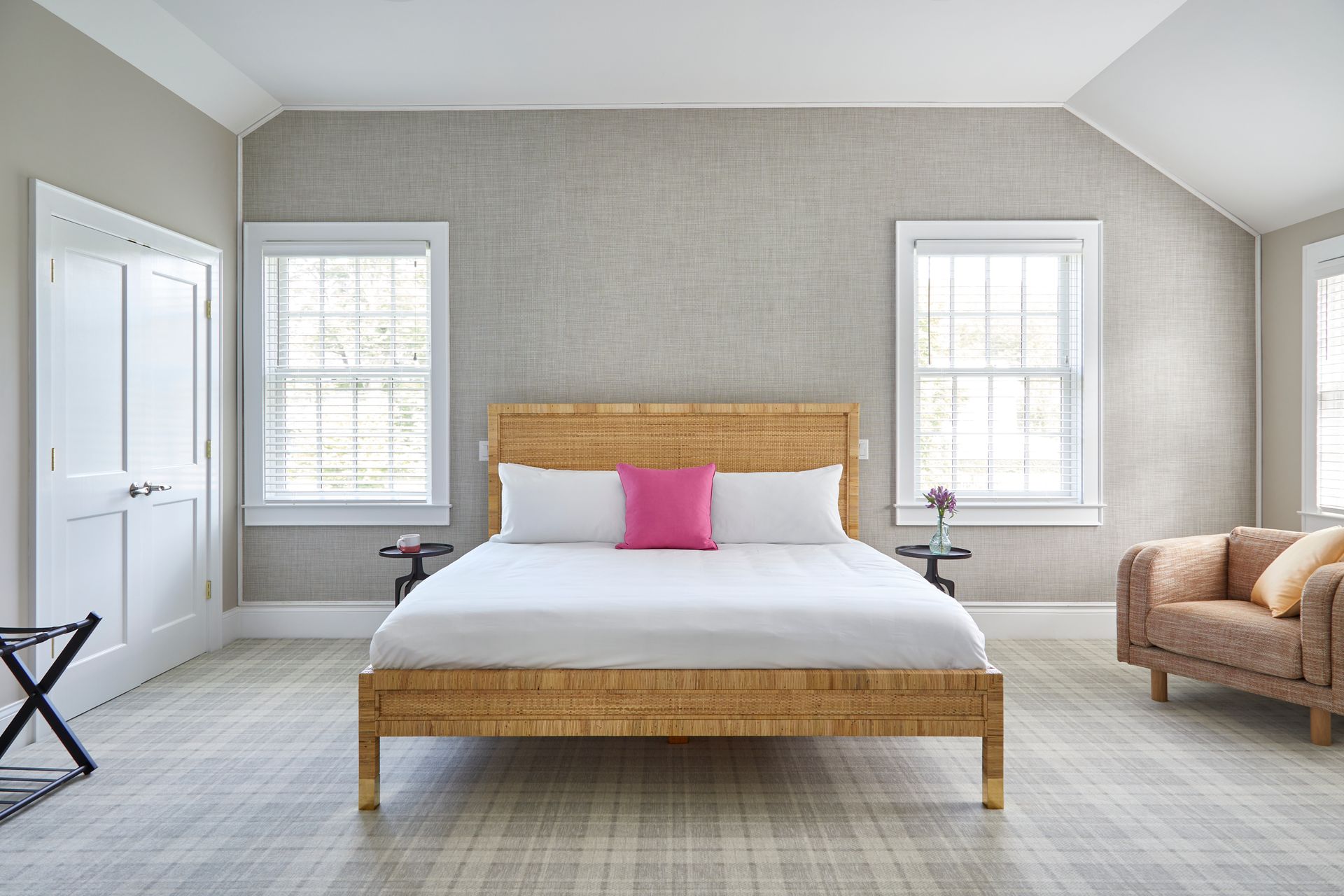 Spacious bedroom with a wicker bed, white walls, two windows, and a beige chair.