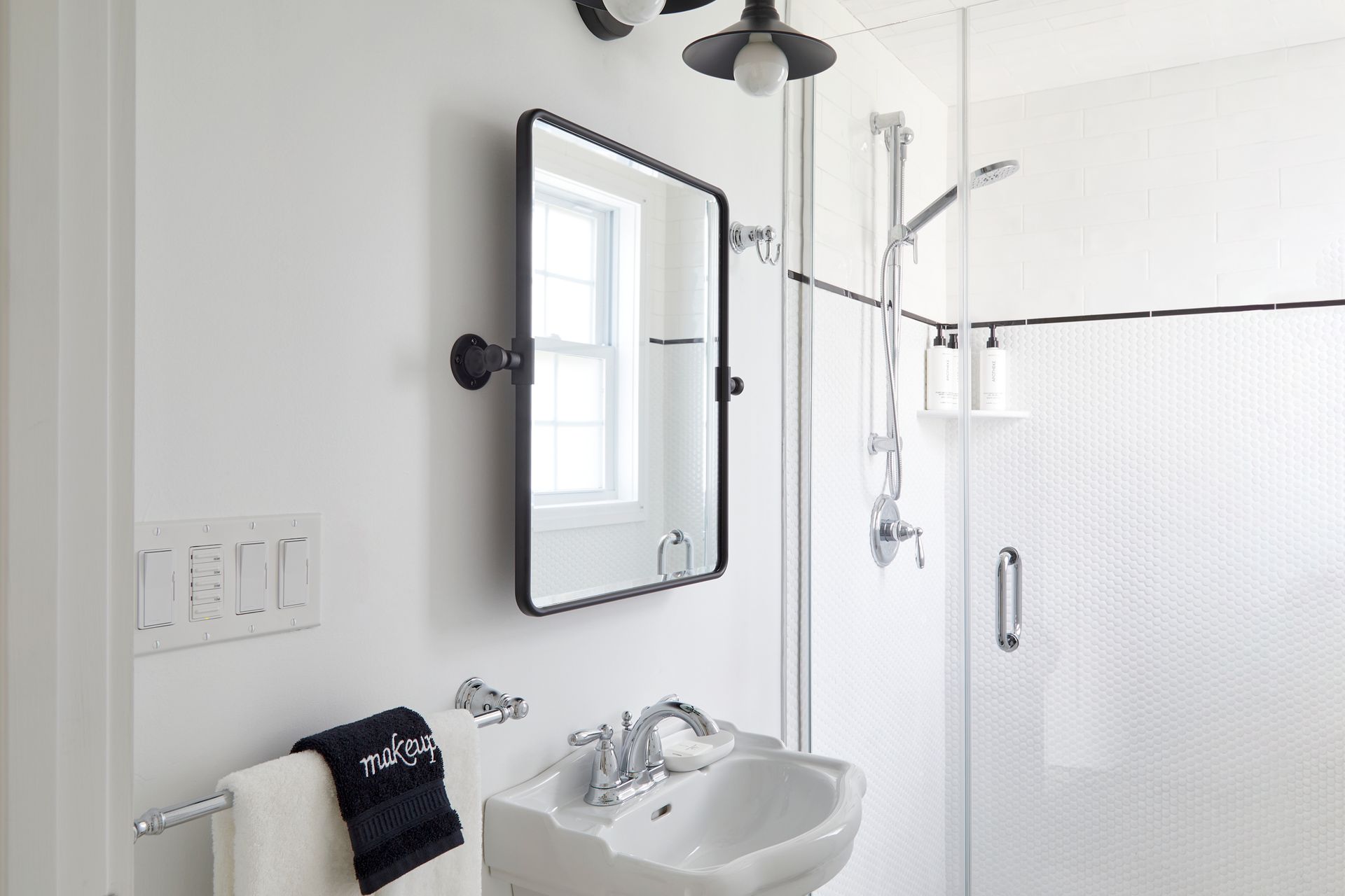 Bright white bathroom with wall mirror, sink, towel rack, and glass shower stall