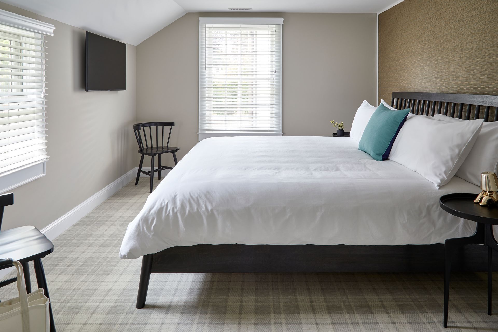 Modern bedroom with a white bed, gray walls, windows, wall-mounted TV, and chair