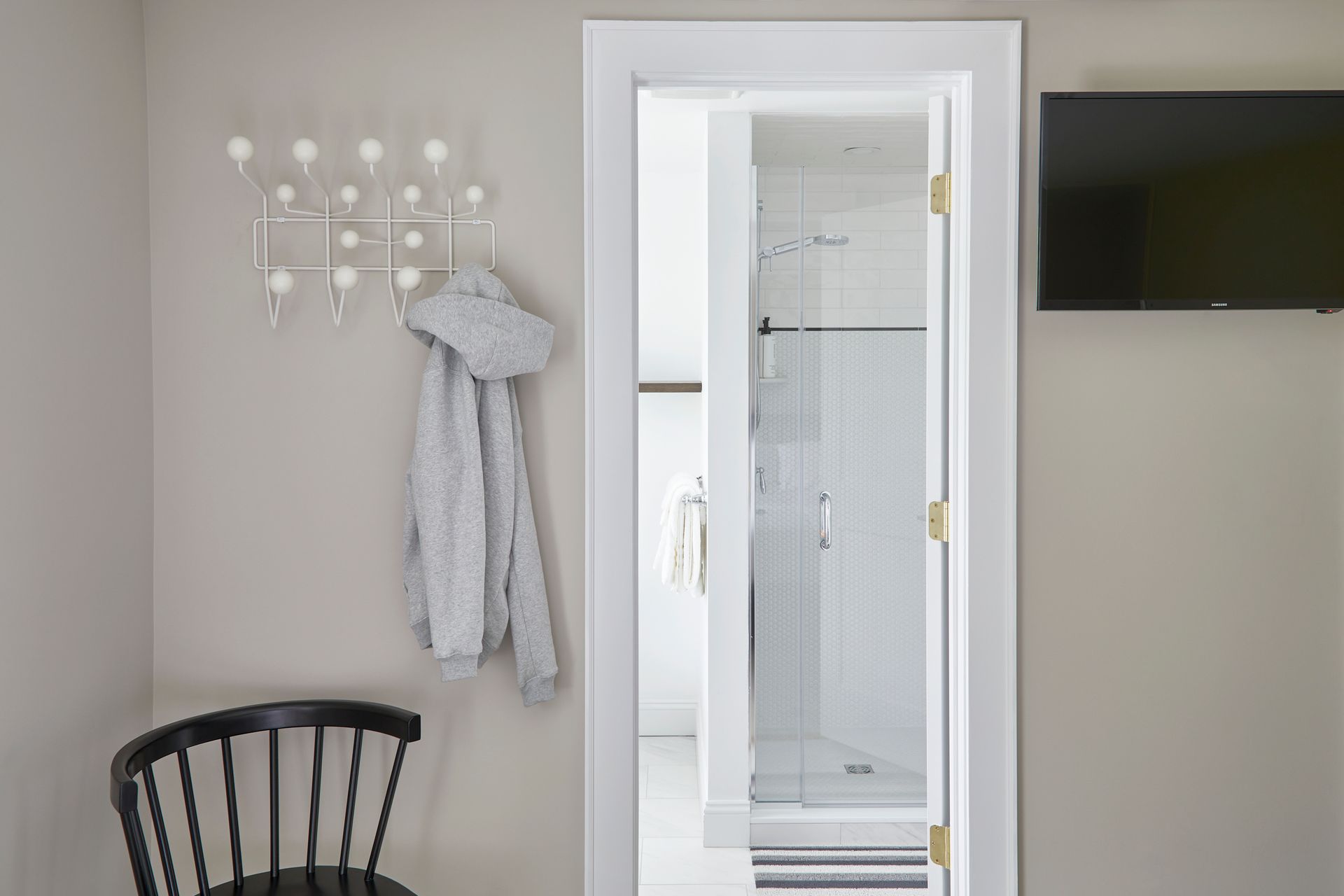 Bathroom doorway with a glass shower visible, coat rack with scarf, and wall-mounted TV.