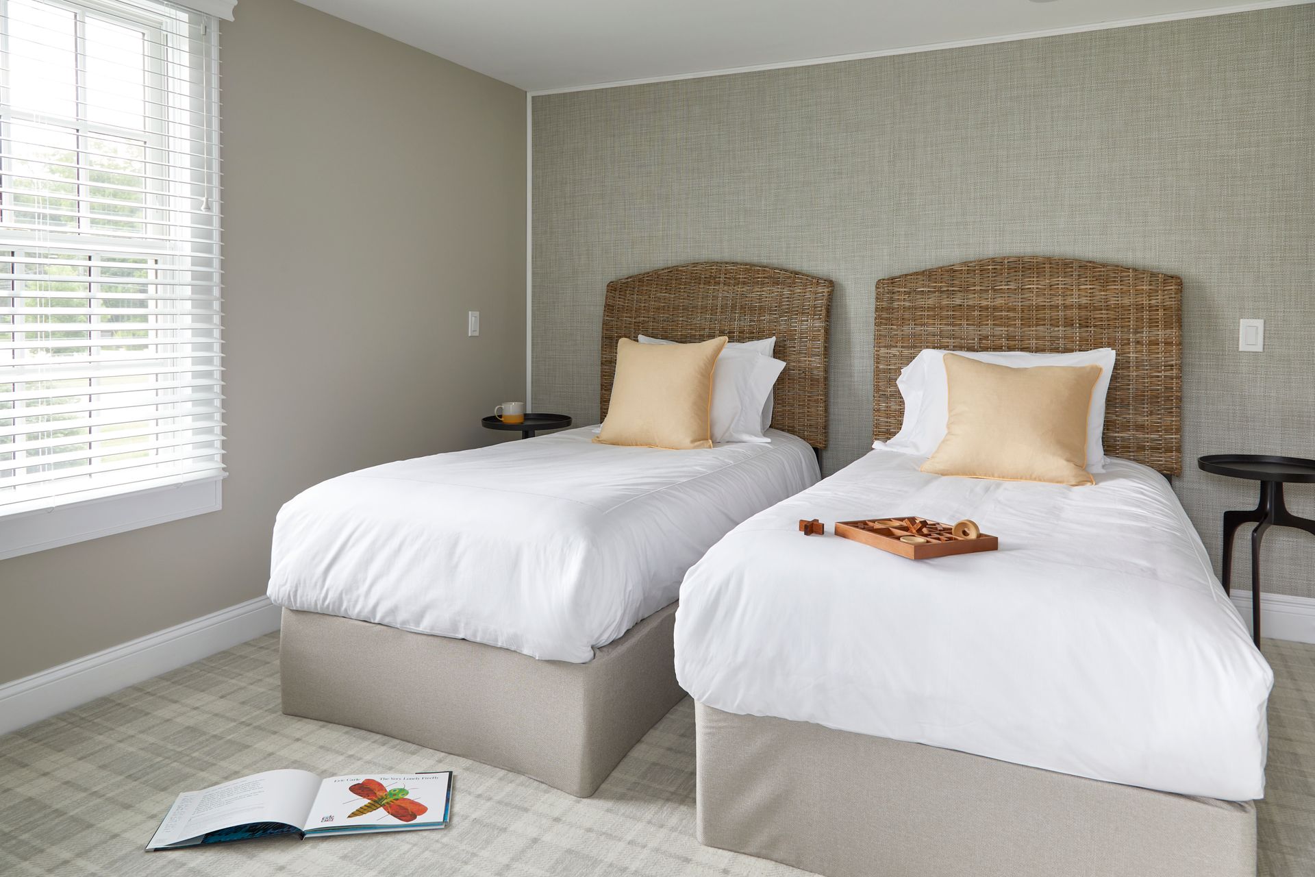 Bedroom with two twin beds, wicker headboards, beige walls, and an open magazine on the carpet.