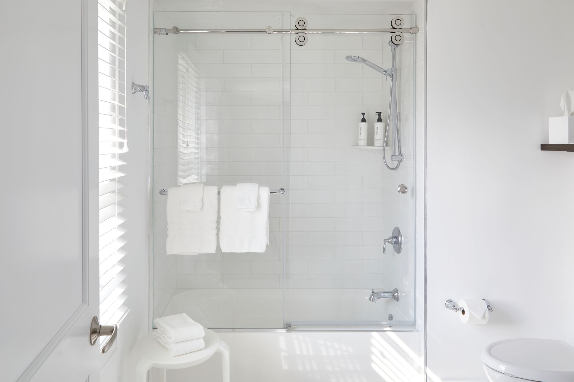 Bright white modern bathroom with glass shower, towel rack, and toilet.