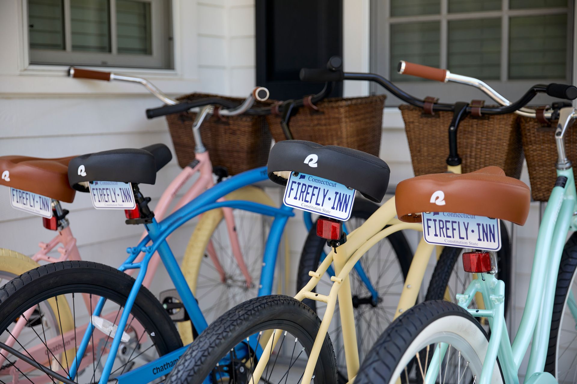 Bicycles with wicker baskets parked in front of a building, including blue, yellow, and mint bikes.