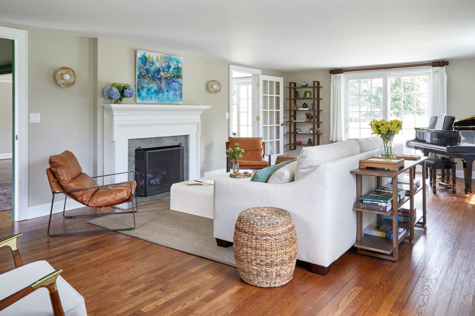 Bright living room with white sofa, fireplace, hardwood floors, and large windows overlooking greenery