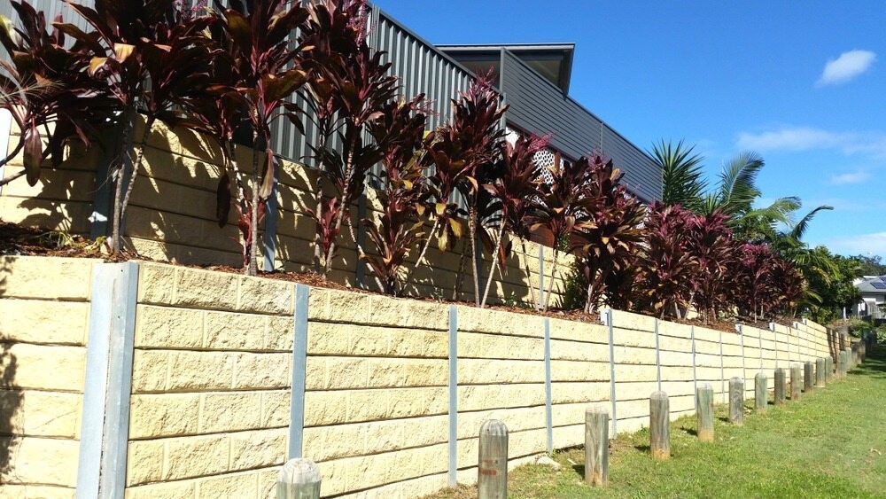 A Brick Wall With Plants Growing on It in Front of a House — Brocksolid Concrete in Pillar Valley, NSW