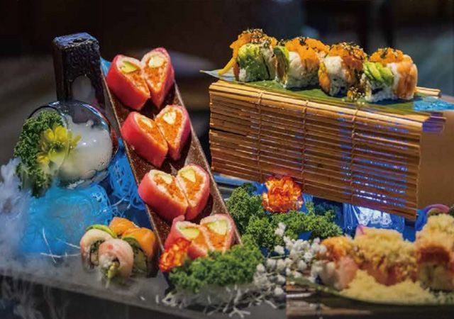Sushi platter with colorful rolls, sashimi, and garnishes arranged on ice and a bamboo stand