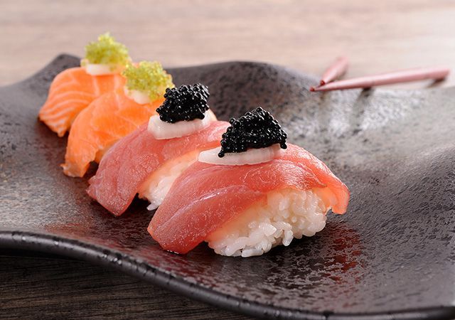 Assorted nigiri sushi with salmon and caviar on a dark ceramic plate