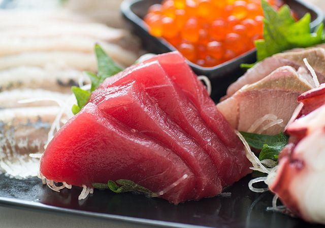 Assorted sushi sashimi platter with red tuna, salmon roe, and white fish on a black tray