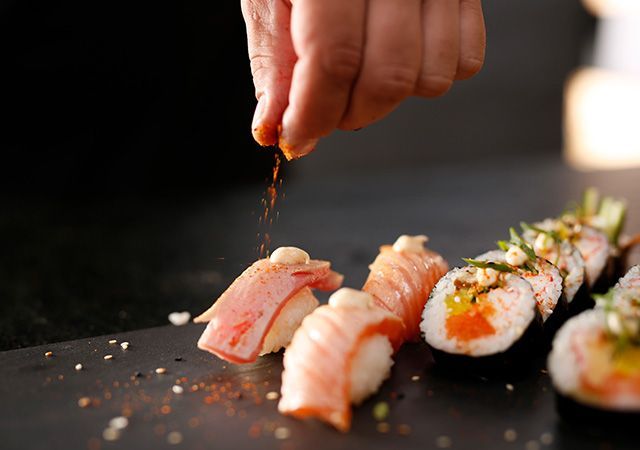 Hand sprinkling seasoning over sushi rolls on a dark plate