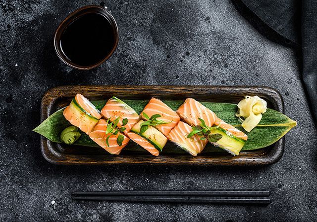 Salmon sashimi on a black plate with green garnish, soy sauce, and chopsticks on a dark table