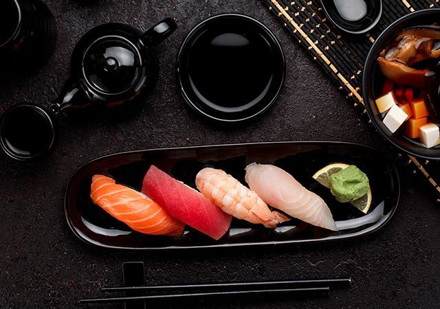 Sushi assortment on a black platter with soy sauce, chopsticks, and tea cups on a dark table
