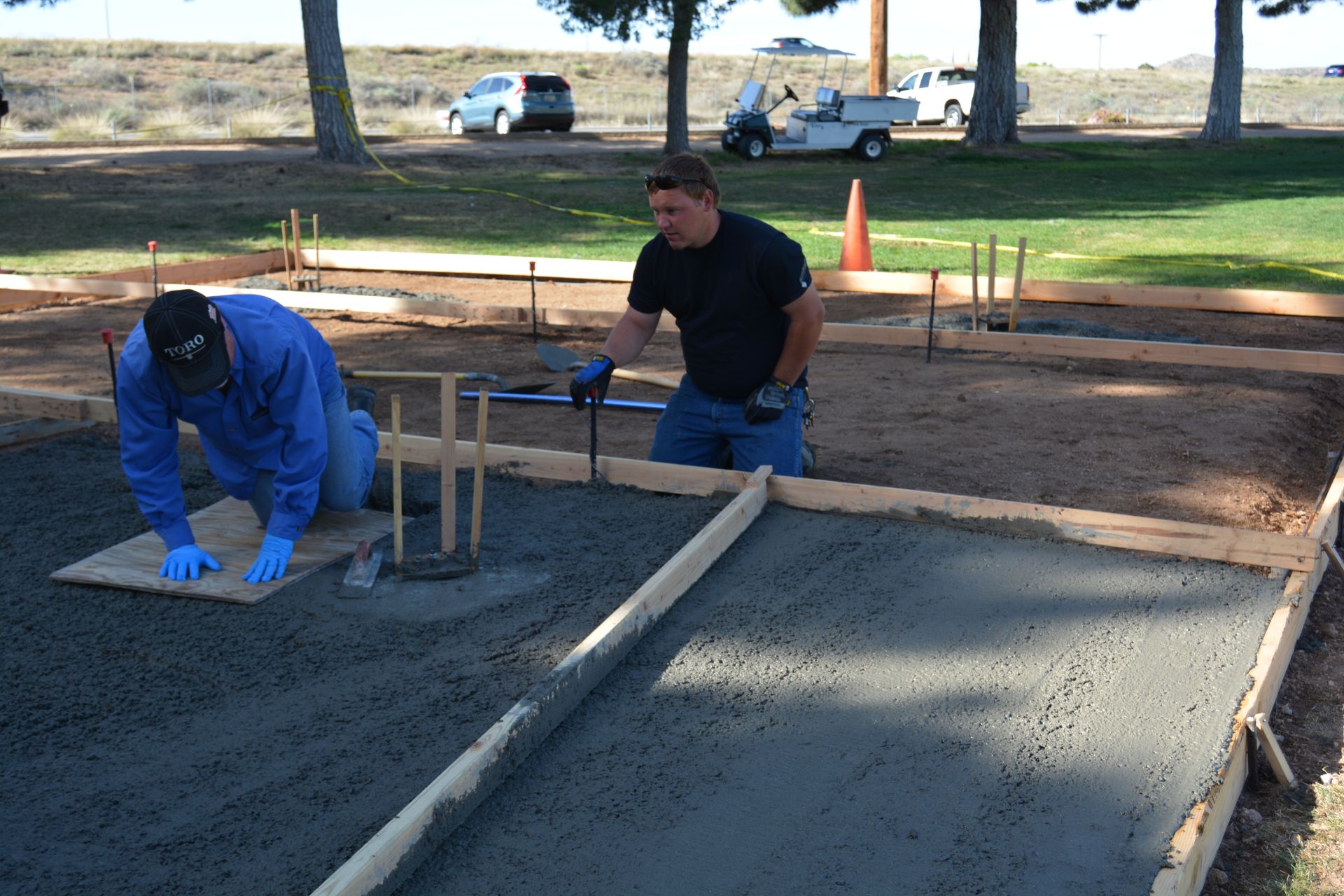 Two men are working on a concrete walkway in a park
