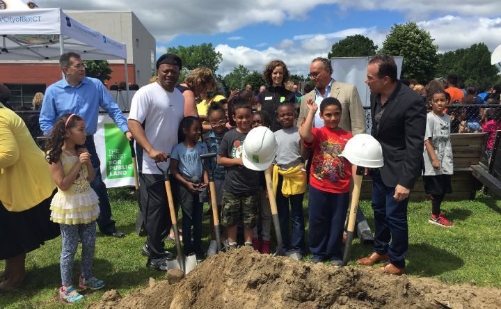 A group of people are standing around a pile of dirt holding shovels.