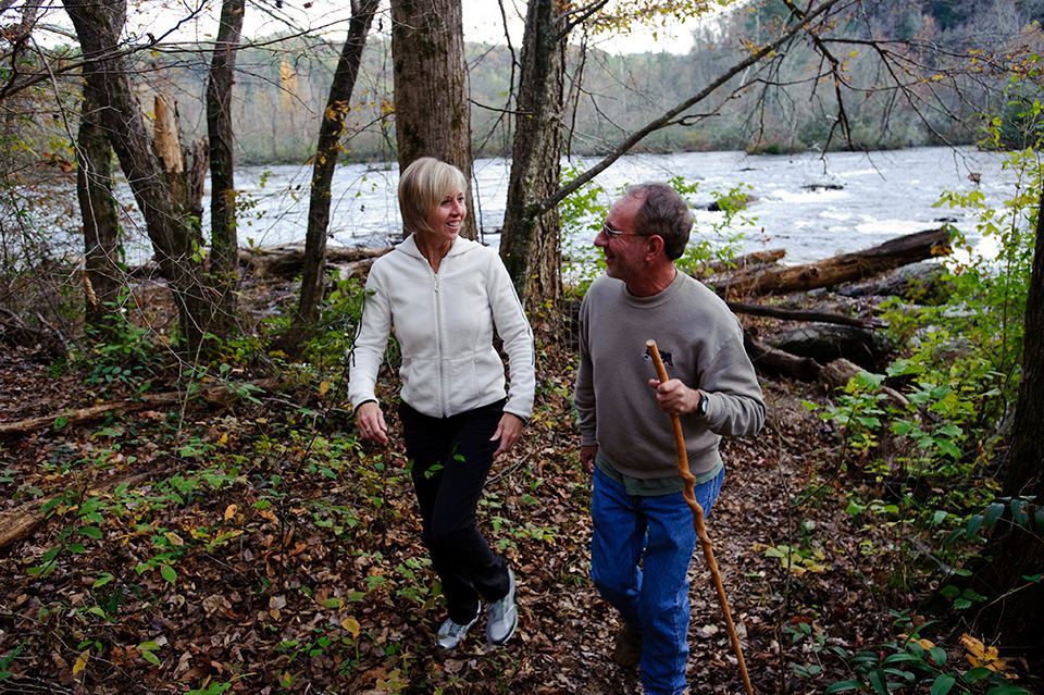 A man and a woman are walking in the woods near a river.
