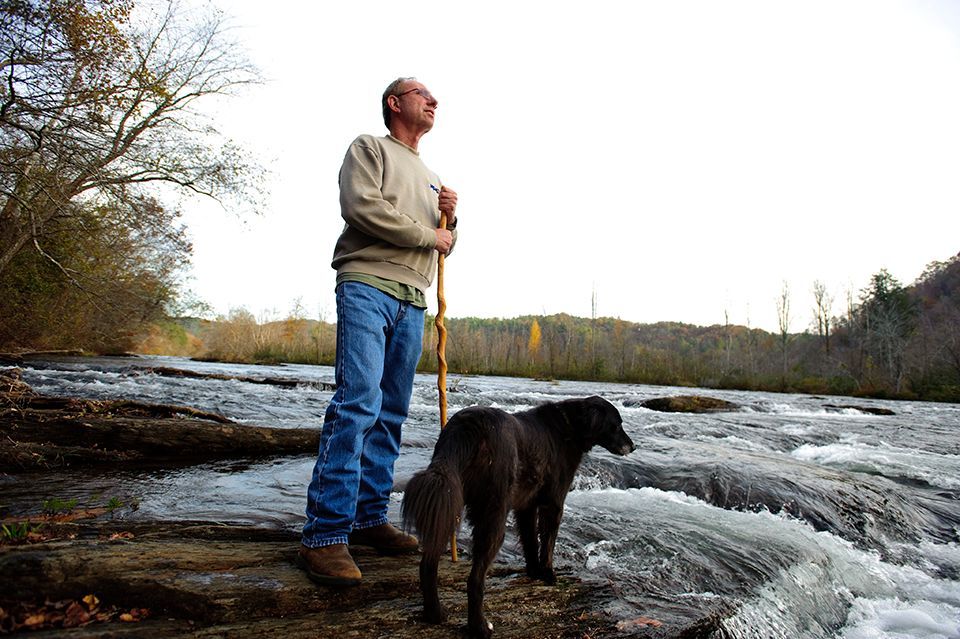 A man with a stick and a dog standing next to a river