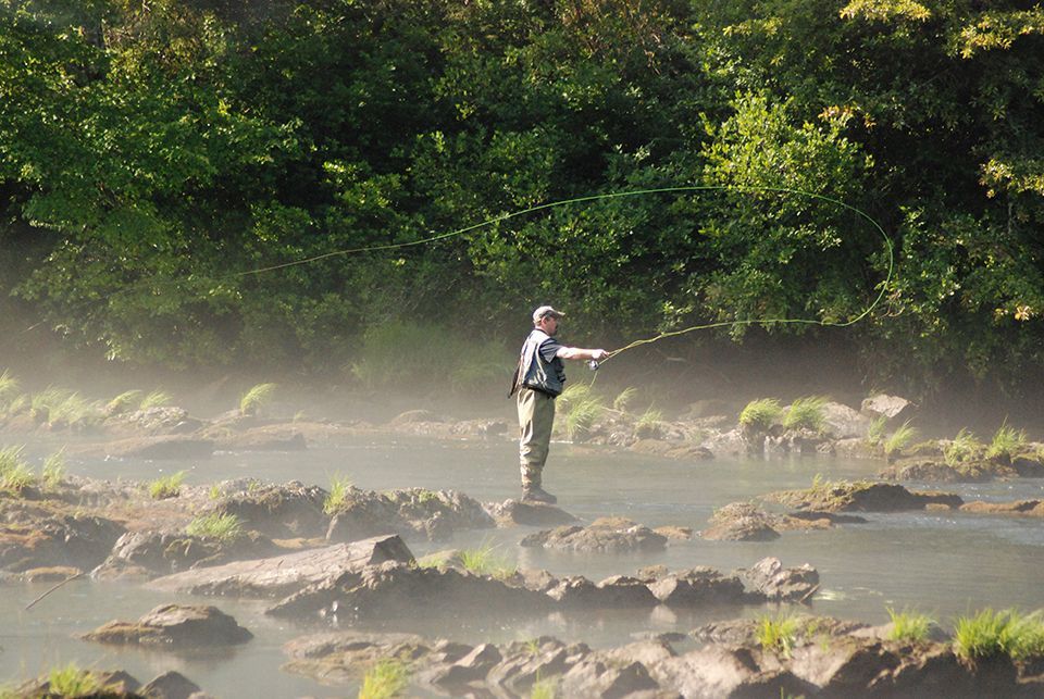 A man is fishing in a river on a foggy day.