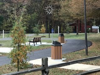 A park with a bench , trash cans , and a wooden fence.