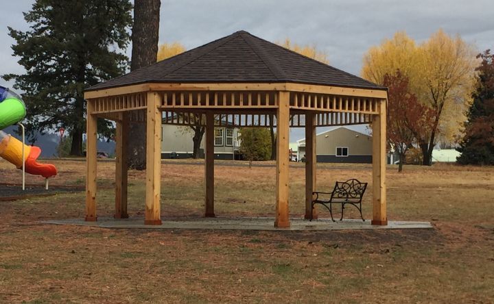 A gazebo in a park with a bench and a slide in the background