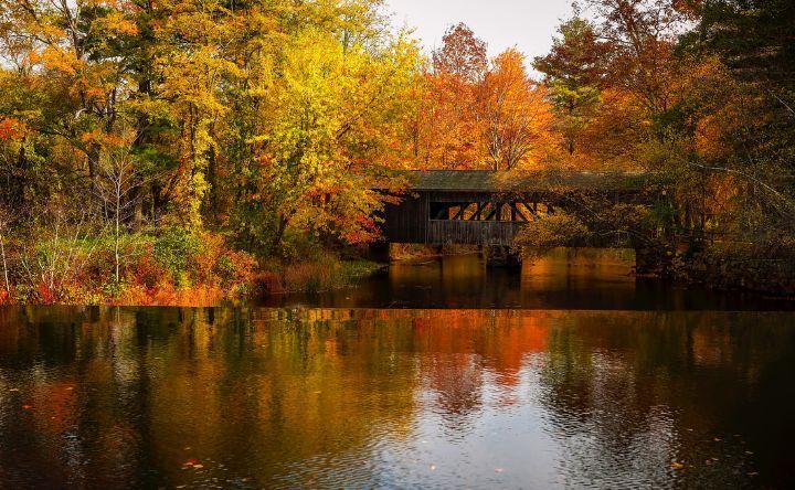 A covered bridge over a lake surrounded by trees in autumn.