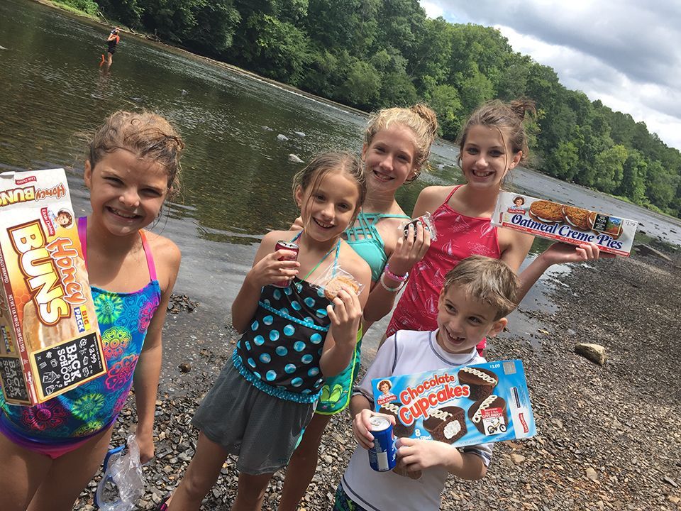 A group of children standing on a beach holding a box of s'mores buns