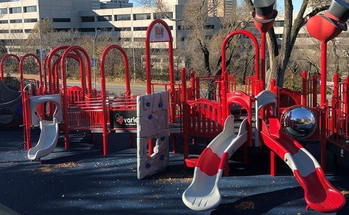 A playground with a lot of red and white equipment and a tree in the background.