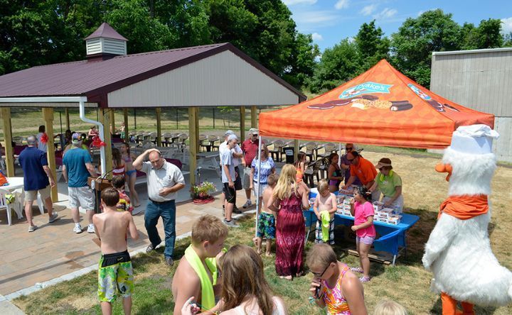 A group of people are standing around a table under an orange tent.