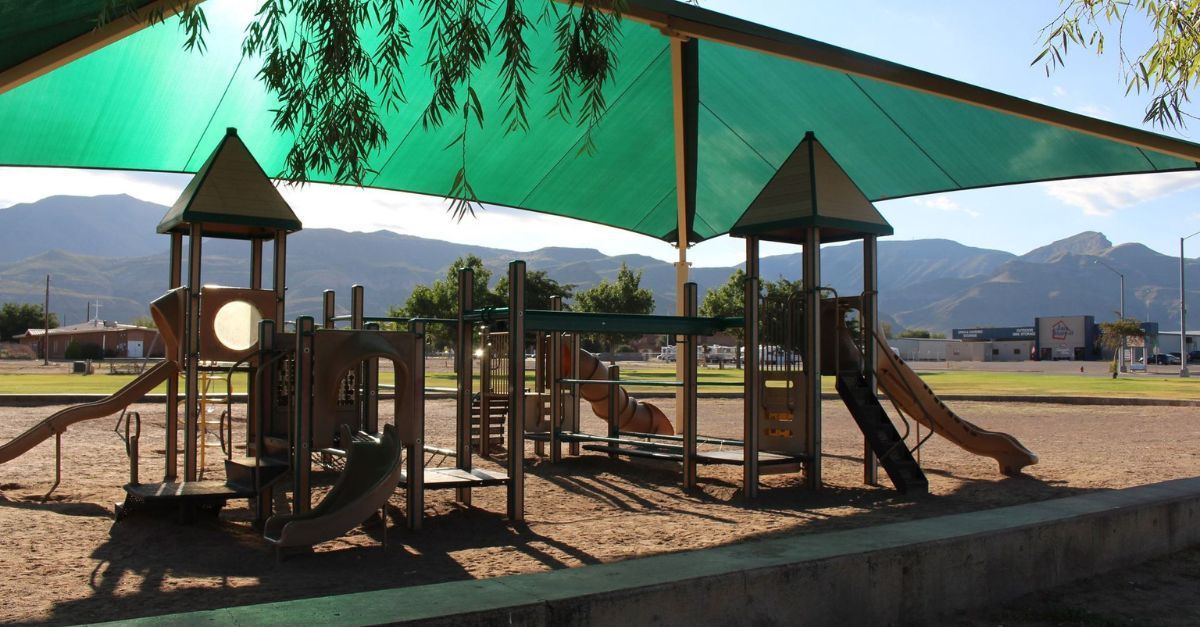 A playground with a green umbrella and mountains in the background