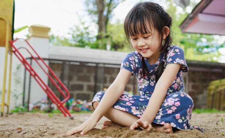A little girl is playing in the sand at a playground.