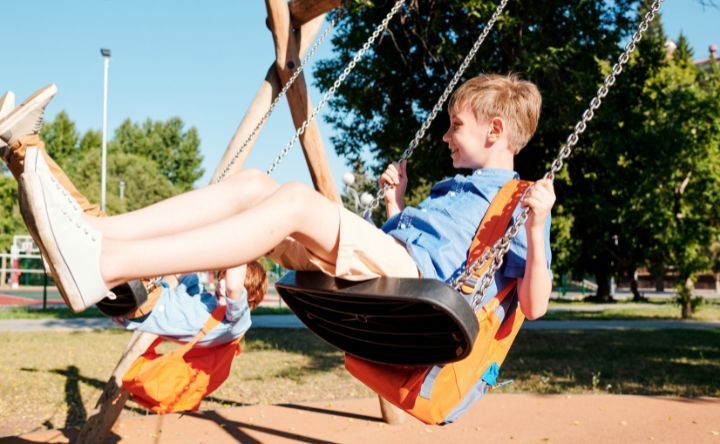 A boy and a girl are sitting on swings in a park.
